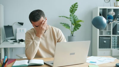A man sitting in front of a laptop is dealing with mental health in the workplace.